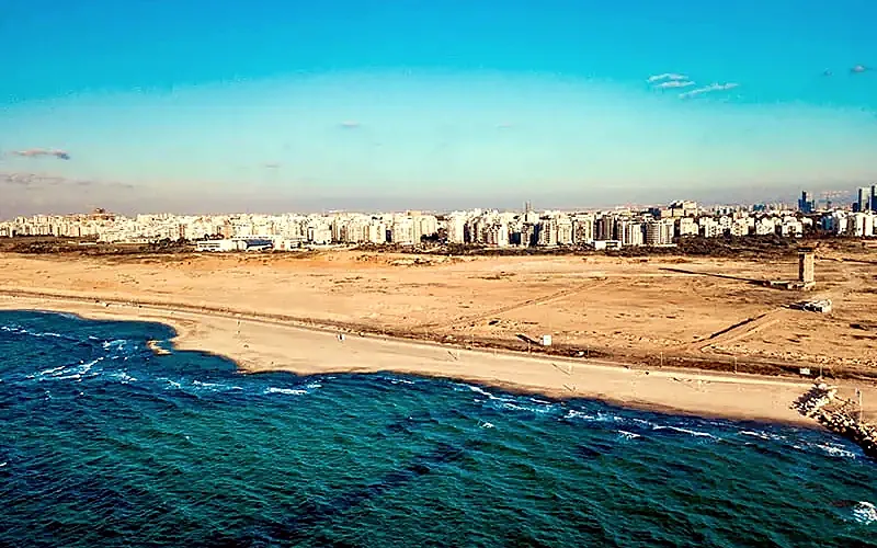 צילום רחפן של חוף, שטח חולי פתוח ובנייני העיר ברקע